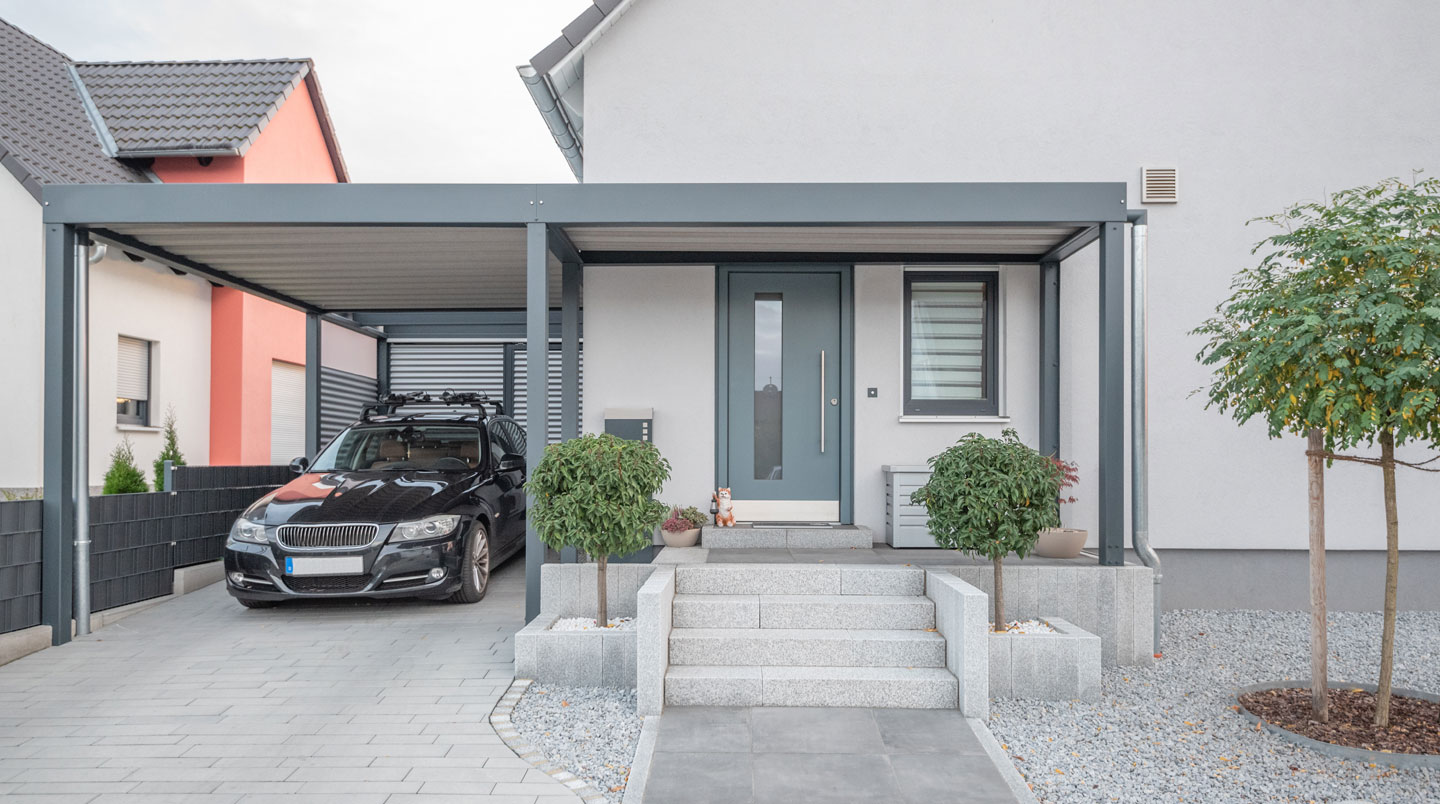 Vue légèrement surélevée d'un petit jardin pavillonnaire français aménagé avec carport moderne, terrasse en bois et délimitations de propriété visibles