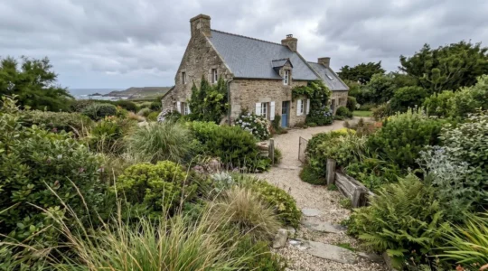 Jardin côtier breton luxuriant avec végétation dense adaptée au climat océanique, maison traditionnelle en pierre et ardoise en arrière-plan